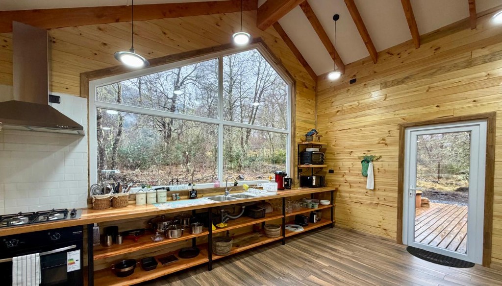 Cocina de Refugio Kürü con mesón de madera, campana y gran ventanal triangular al bosque