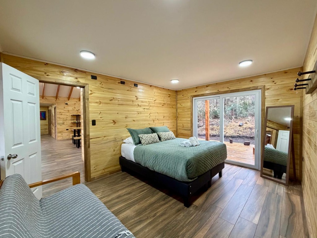 Dormitorio principal de Refugio Kürü con cama, espejo y puerta abierta hacia el living