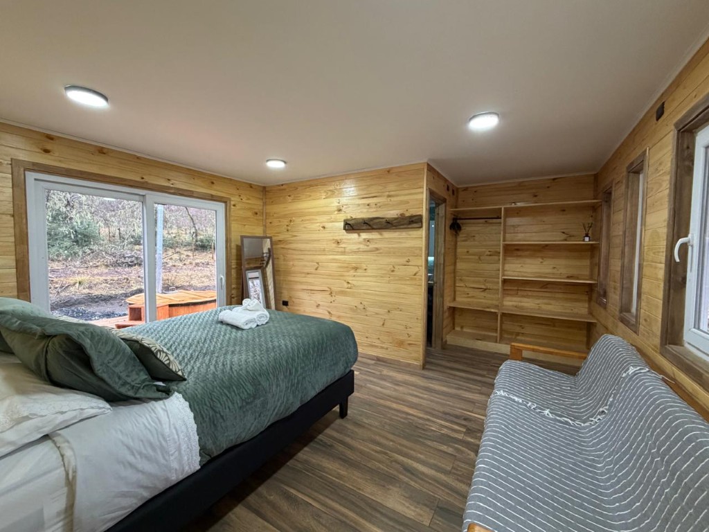 Dormitorio principal de Refugio Kürü con sofá cama, clóset y ventanal hacia el bosque