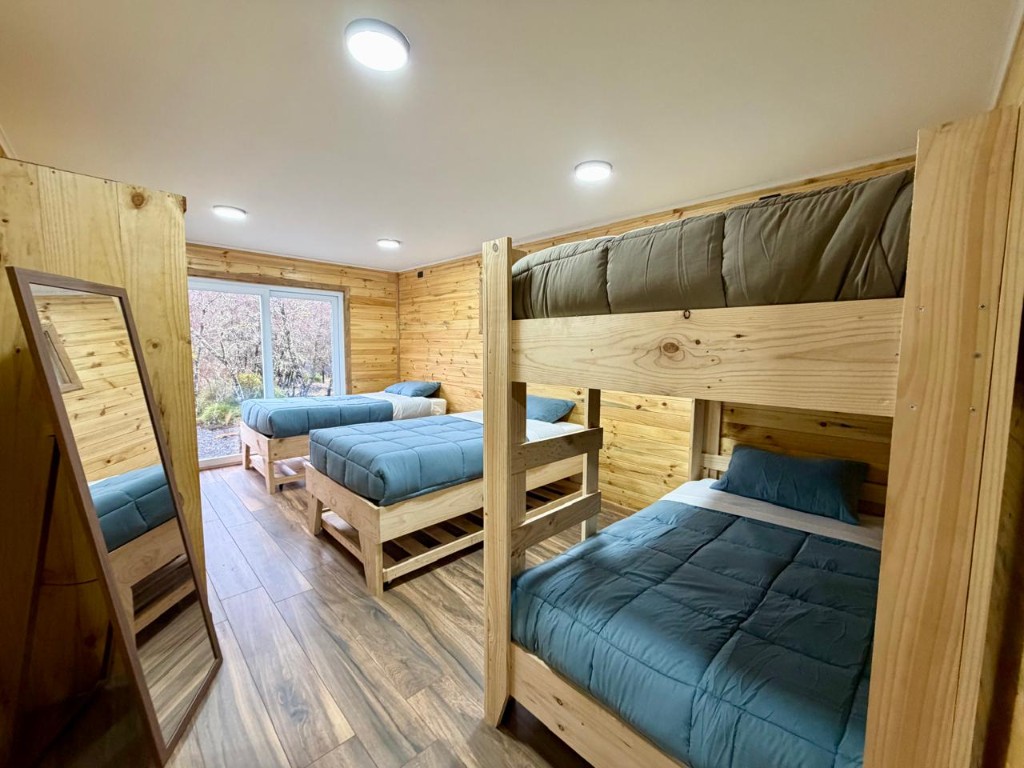 Habitación de Refugio Kürü con literas, camas individuales y ventanal hacia el bosque