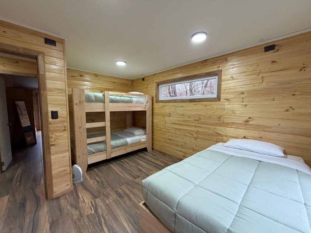 Habitación de Refugio Kürü con cama matrimonial, literas de madera y ventanal alto