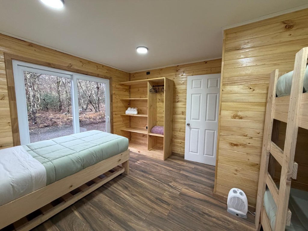 Habitación de Refugio Kürü con cama individual junto al ventanal, clóset y literas