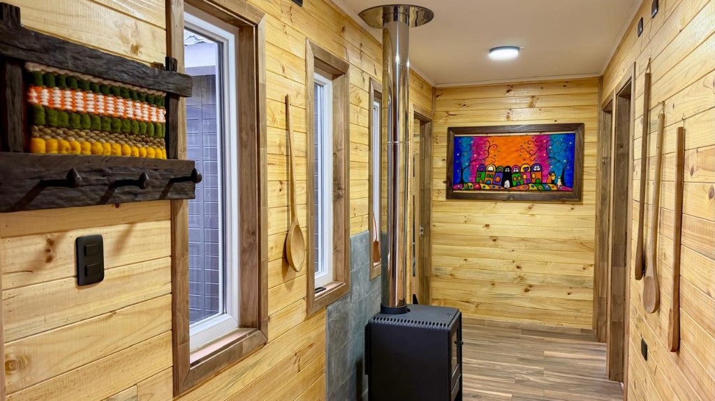 Pasillo de Refugio Kürü con estufa a leña, ventanas y tejidos en la pared de madera